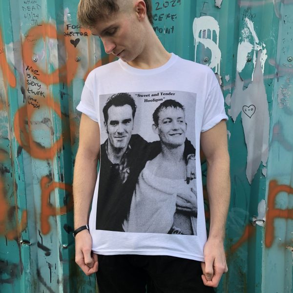 A male model wearing the 'Sweet and Tender Hooligan' T-shirt with a green metal wall behind him which has graffiti on it