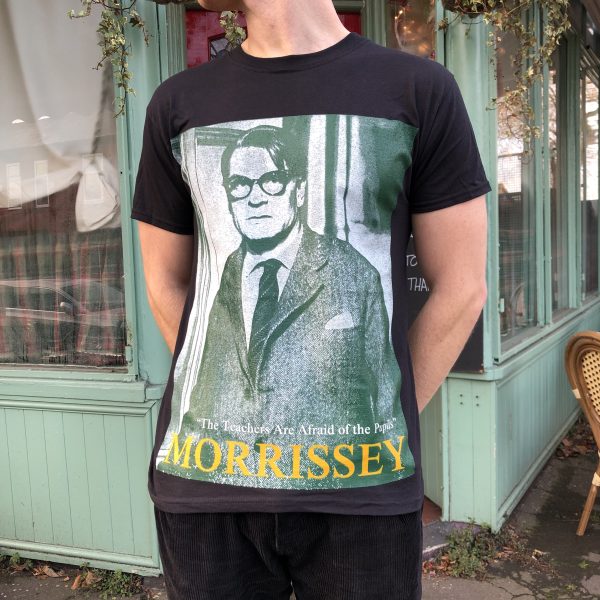 A male model wearing the 'Teachers' T-shirt with a cafe behind him
